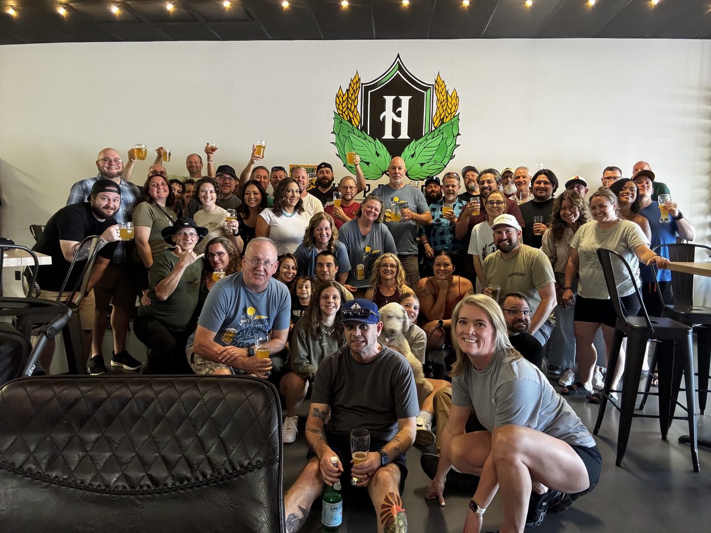Large group celebrating at Hopsology under the crest mural